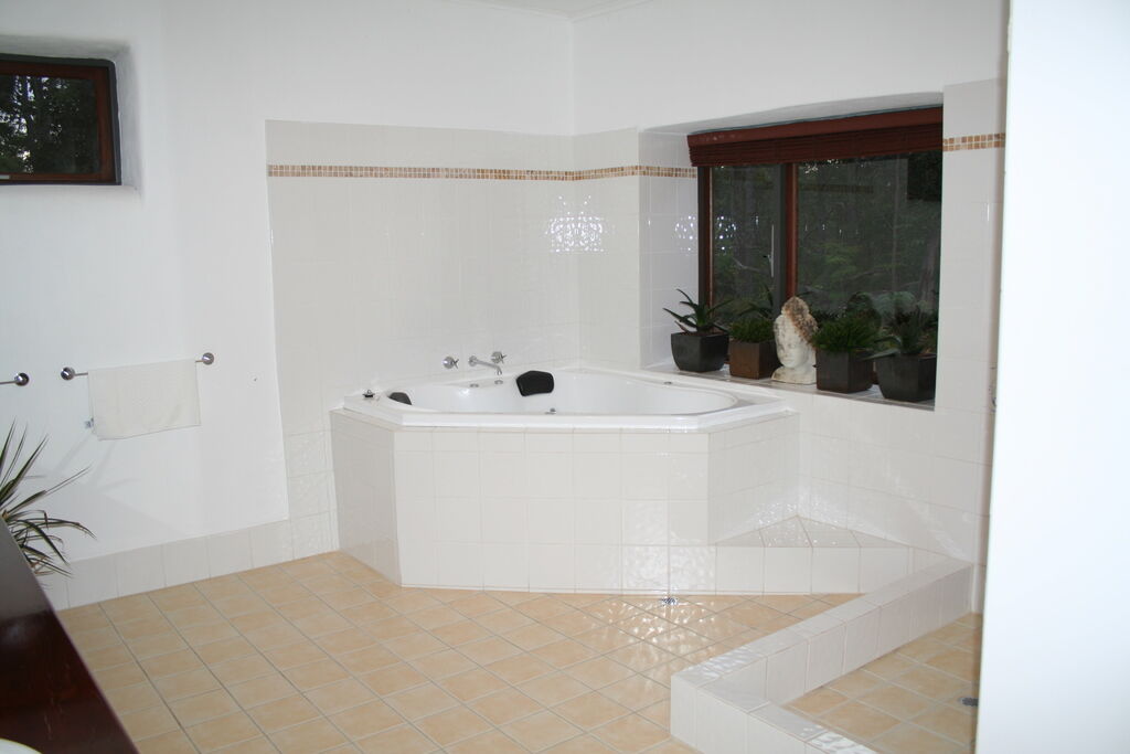 A bright bathroom with a white corner tub beneath a window and light tiled floors