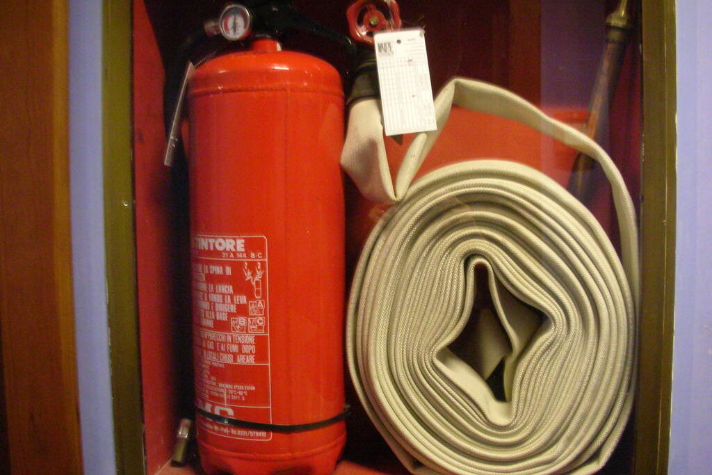 A red fire extinguisher and a rolled fire hose ready inside a wall cabinet