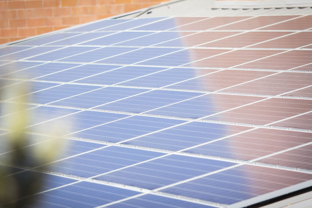 Rows of blue solar panels on a roof beside a brick wall